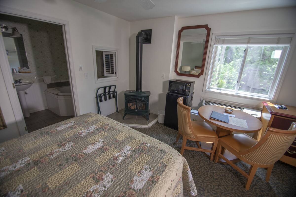 A bedroom with a bed, a desk, a chair, a microwave, a heater, a window, and a bathroom.