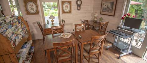 A dining area with wooden tables and chairs, a computer desk with a monitor, keyboard, and mouse, and a wall clock.