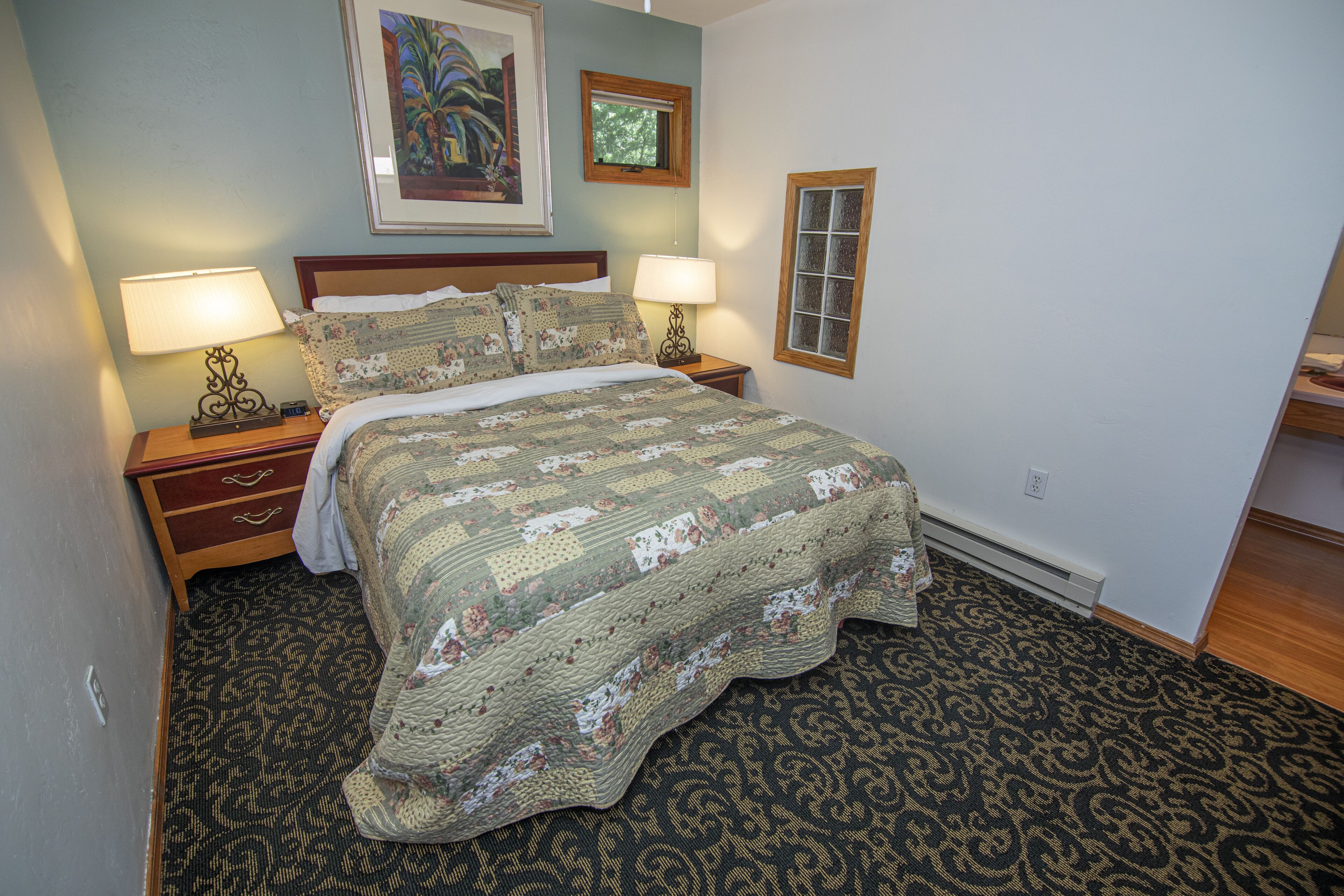 A neatly made bed with a floral quilt, two bedside lamps, a nightstand, and a framed picture on the wall.