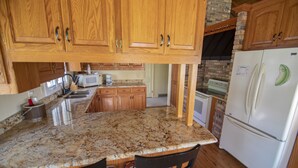 A kitchen with wooden cabinets, a granite countertop, a refrigerator, and a microwave. - Coachlite Inn (Sister Bay)