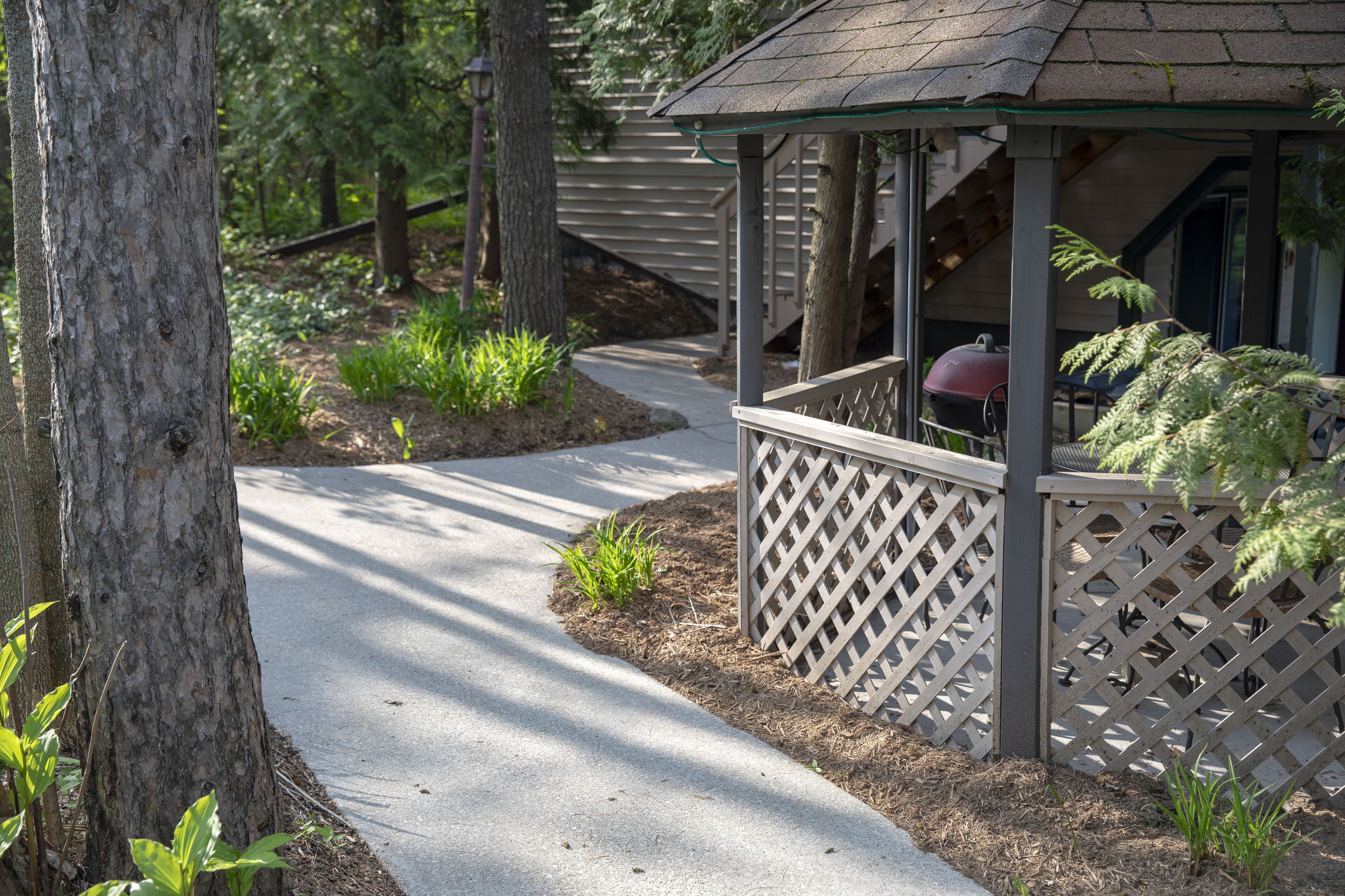 A covered outdoor area with a wooden deck, a barbecue grill, and a pathway leading to a building.