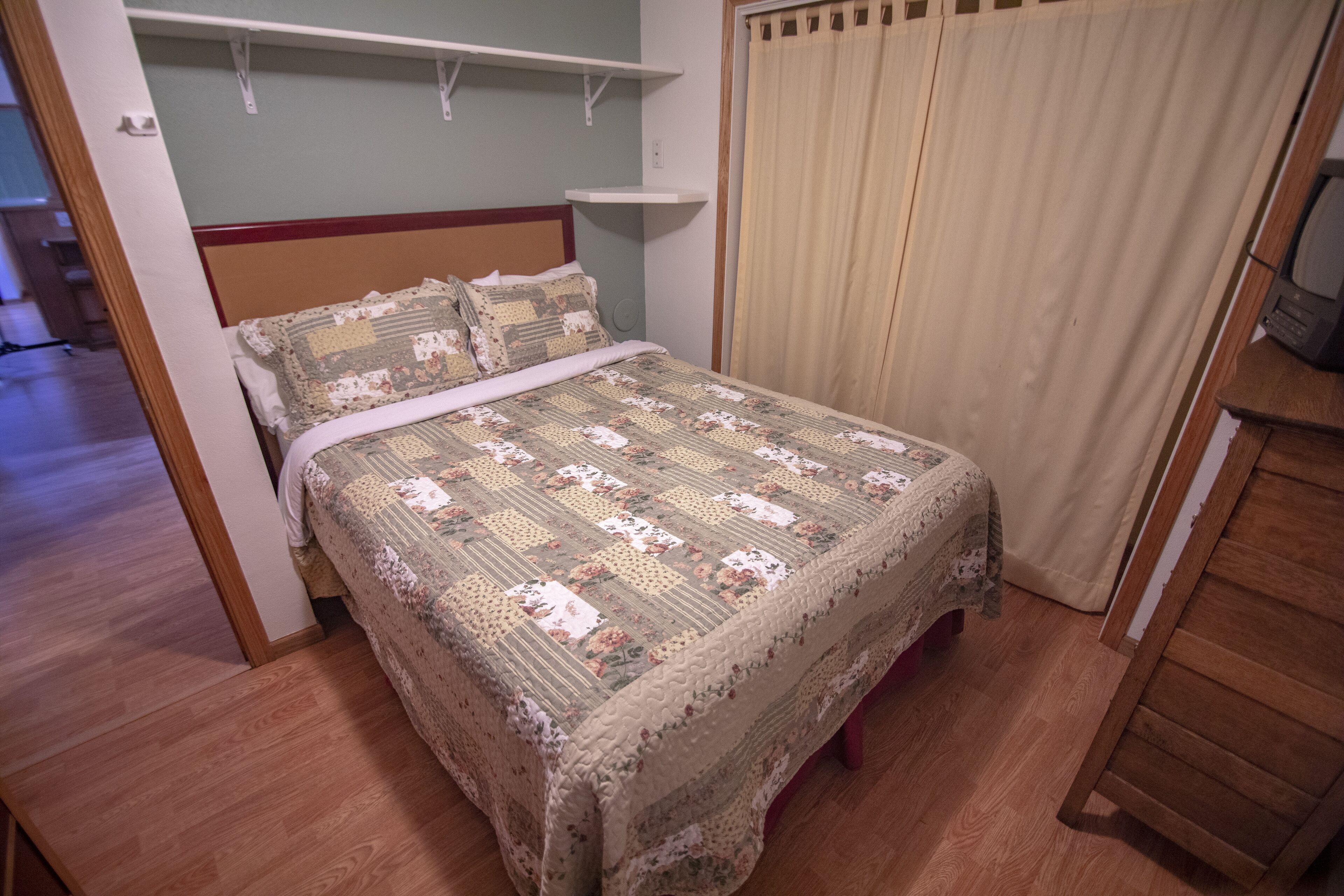 A bedroom with a bed, a wooden floor, a curtain, and a television on a wooden stand.