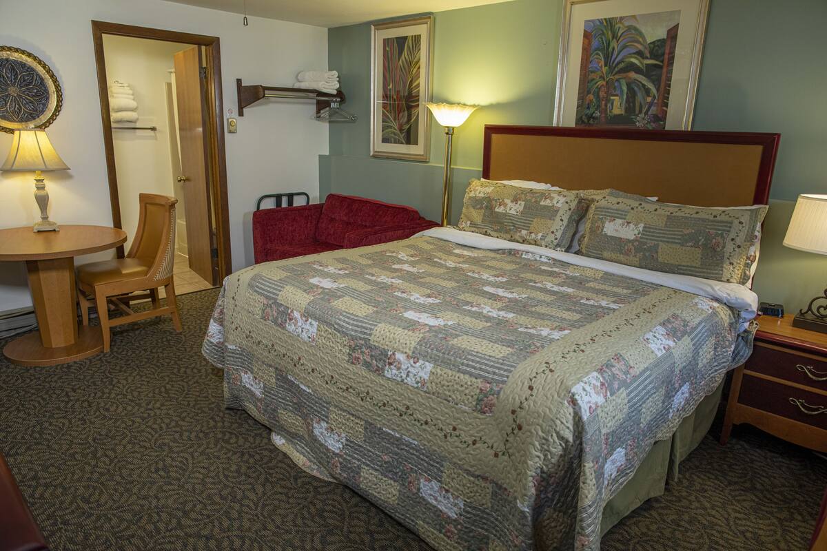 A hotel room with a large bed, a desk with a chair, a lamp, and a painting on the wall.