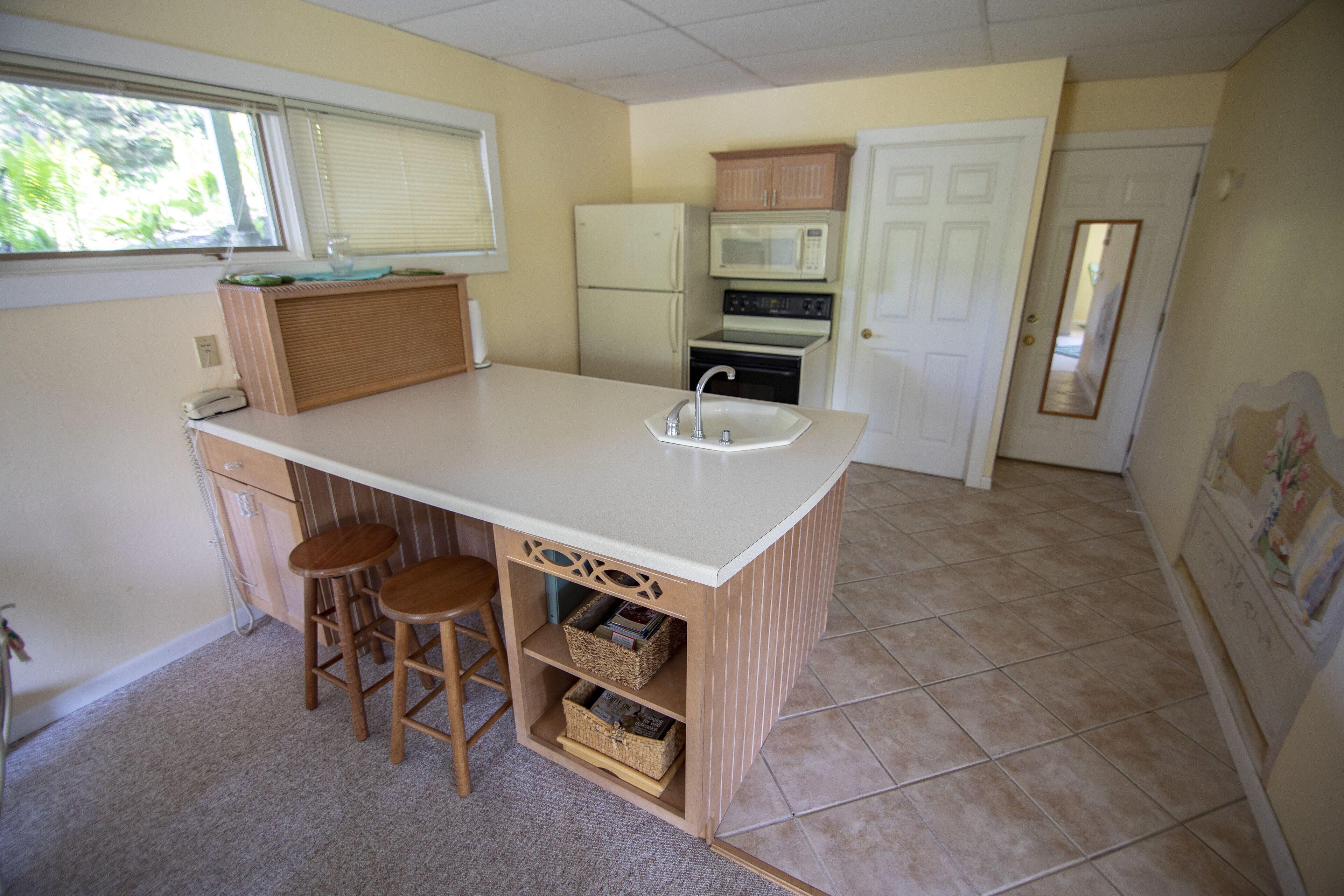 Una cocina compacta con encimera blanca, dos taburetes de madera, un lavaplatos empotrado y un microondas sobre la estufa.