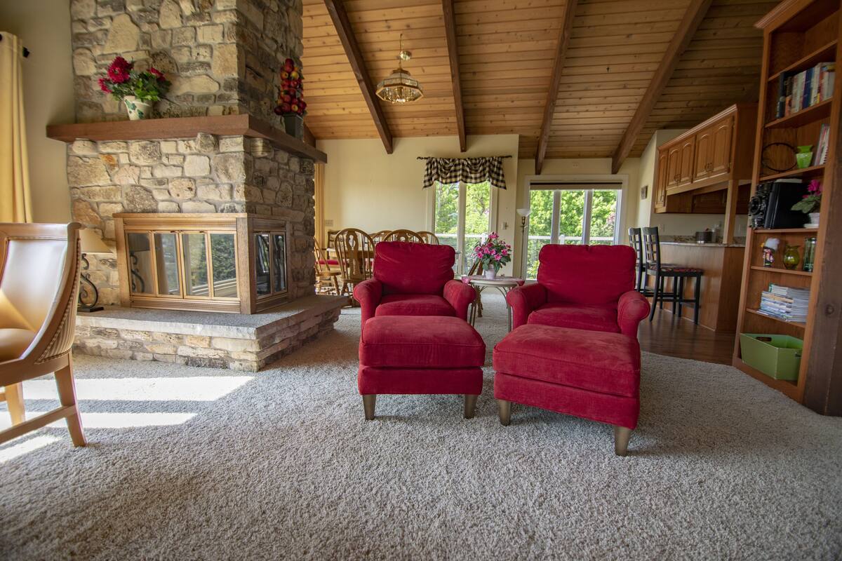A cozy living room with a stone fireplace, red armchairs, and a wooden ceiling.