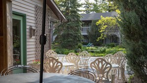 An outdoor patio with round tables and chairs, a wooden fence, and a house in the background.