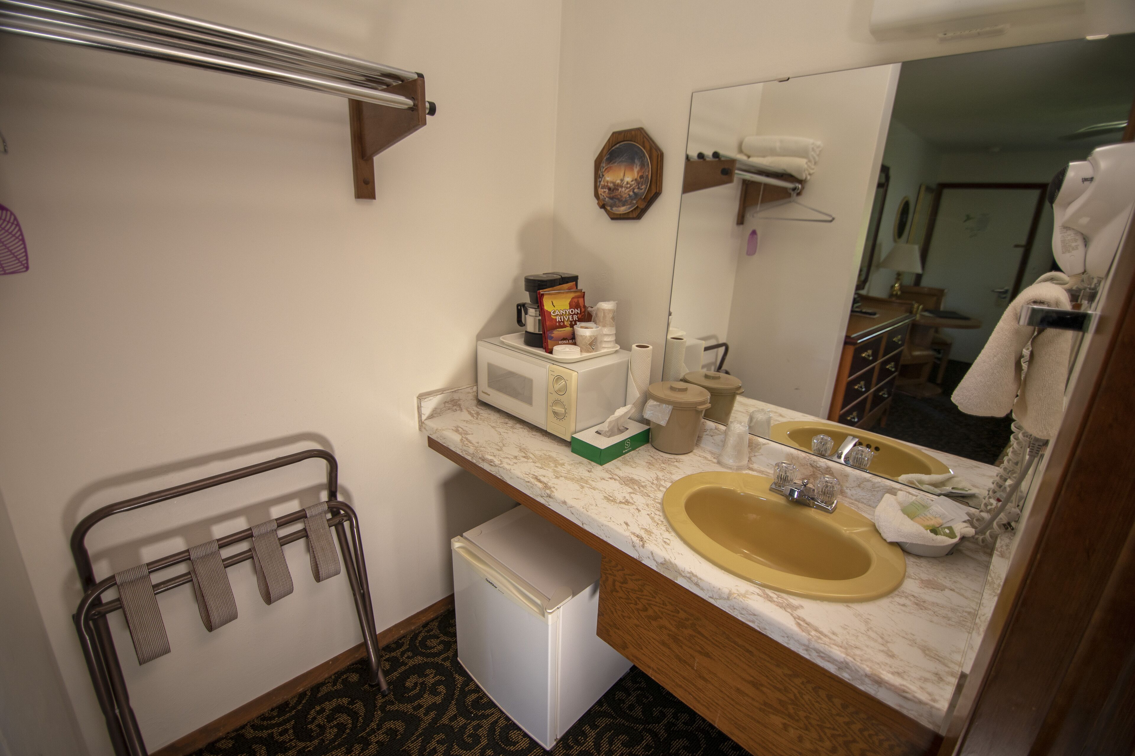 A compact hotel bathroom with a sink, mirror, towel rack, and a small refrigerator.