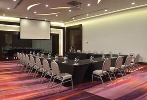 Un salón de conferencias con una larga mesa, sillas y una pantalla para proyector.
