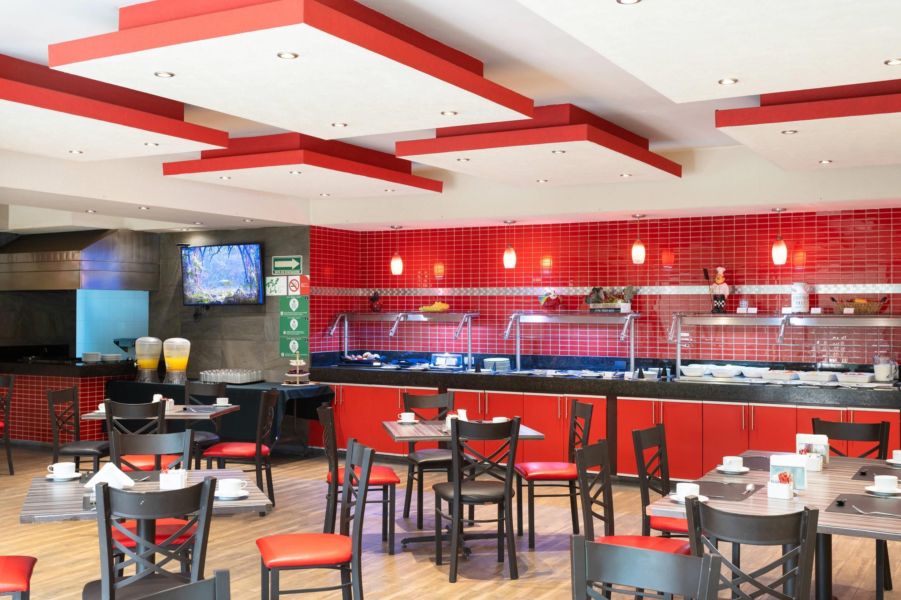 A restaurant with red and white decor, a counter with a beverage dispenser, and multiple tables and chairs.