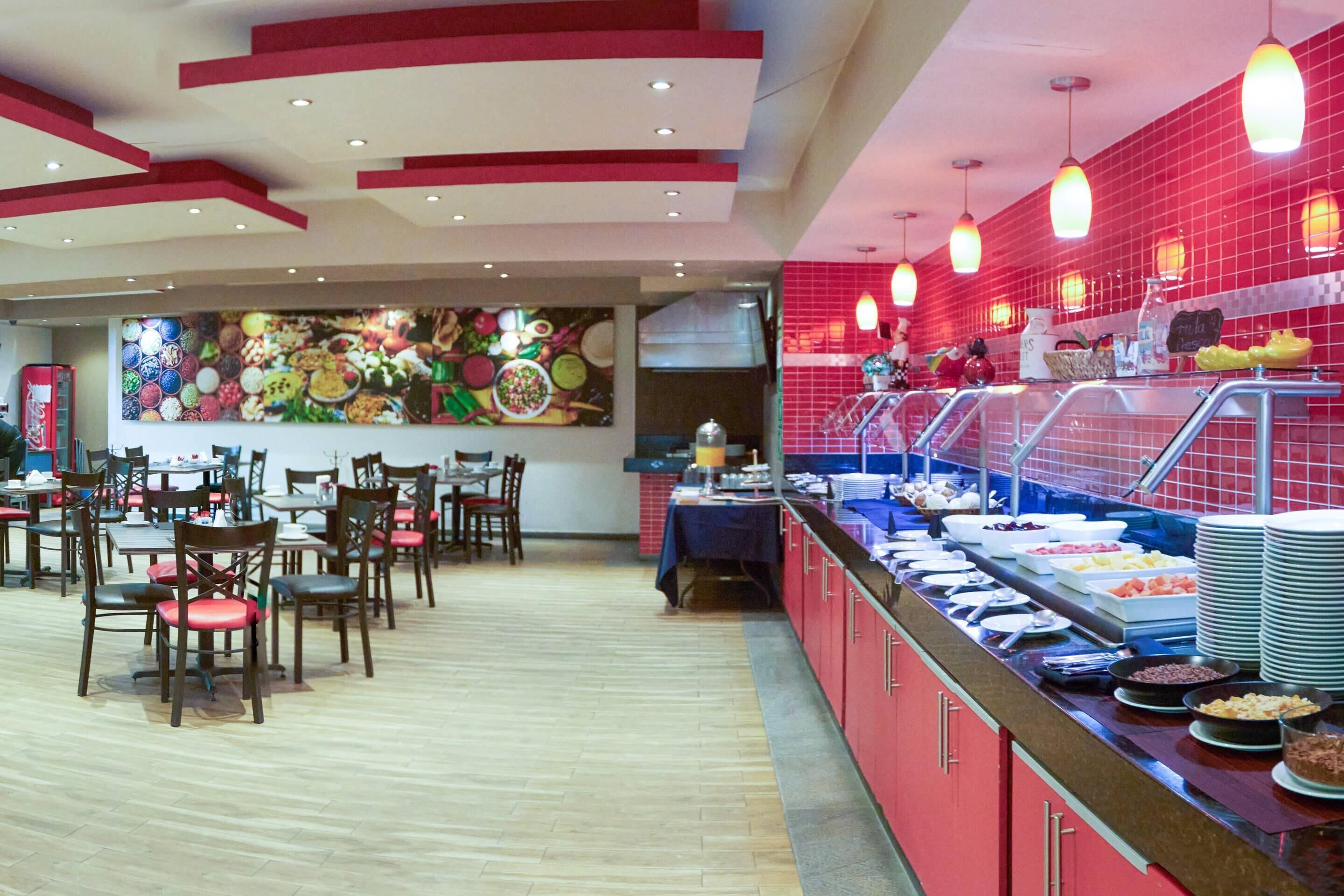 Un área de bufé con diferentes opciones de comida, un espacio de comedor con mesas y sillas, y un mural de pared llamativo.