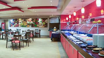 Un área de bufé con diferentes opciones de comida, un espacio de comedor con mesas y sillas, y un mural de pared llamativo.