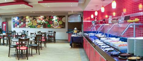 Un área de bufé con diferentes opciones de comida, un espacio de comedor con mesas y sillas, y un mural de pared llamativo.