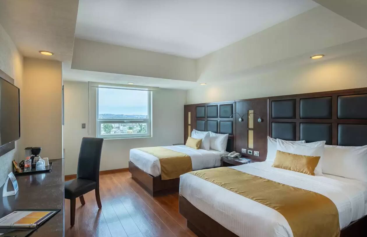 Habitación de hotel con dos camas, un escritorio, una silla y ventana con vista.