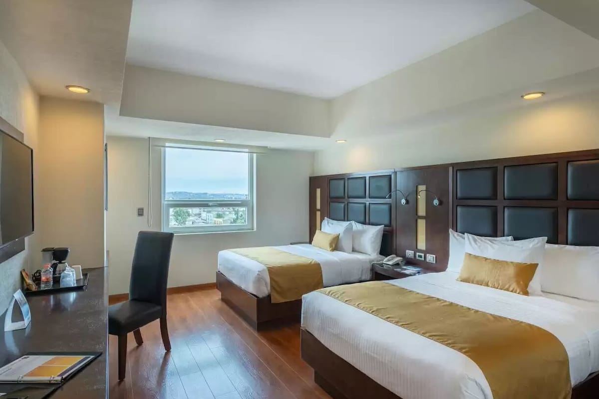 Habitación de hotel con dos camas, un escritorio, una silla y ventana con vista.
