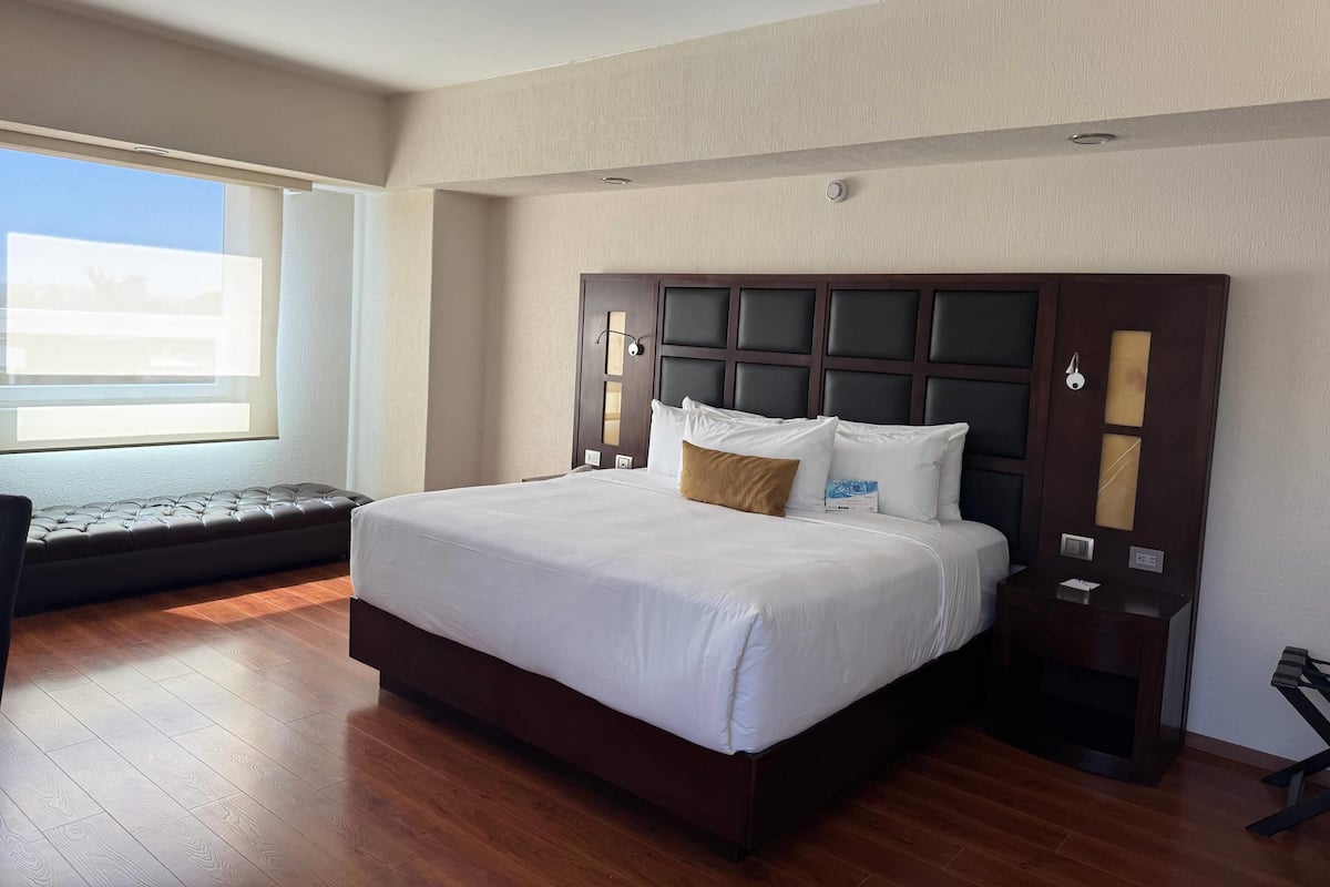 Una habitación de hotel moderna con una cama grande, suelo de madera, un banco empotrado y una ventana con vistas.