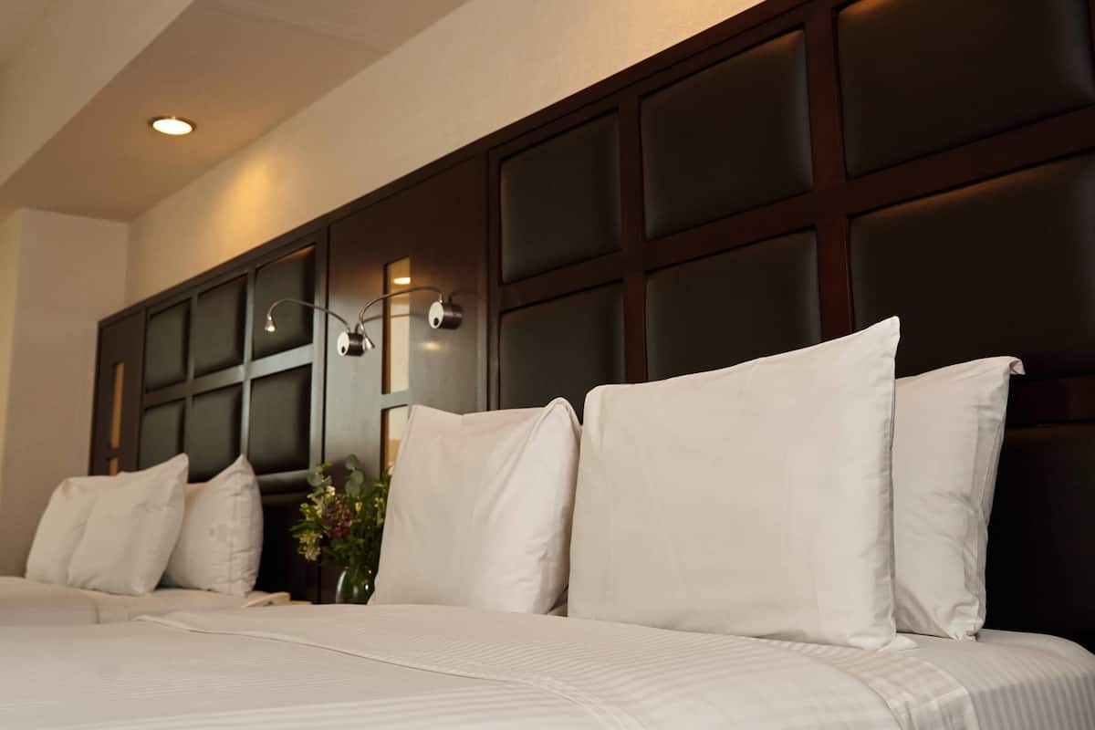 Una habitación de hotel con una cama grande, cabecera oscura y una lámpara fijada a la pared.