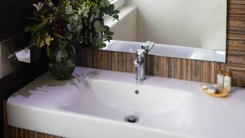 A bathroom sink with a mirror above it, a vase with flowers, and a small wooden tray with bottles.