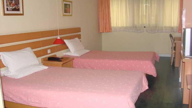 Et hotelværelse med to senge, hver med et rosa sengetæppe, en træsenggavl, et natbord med lampe og et fjernsyn.
