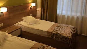 A hotel room with two beds, a green accent wall, a window with curtains, and a wall-mounted air conditioner. - Ceramica Hotel (Iasi)