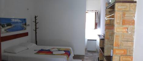 A bedroom with a bed, a painting, a wooden headboard, a white wall, a brick wall, and a window.