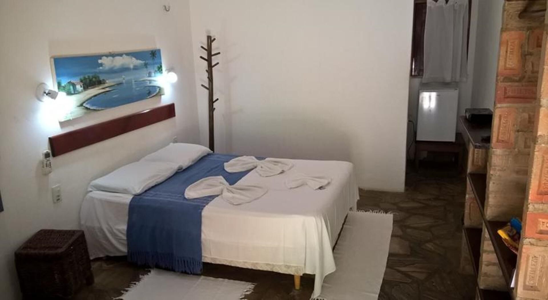 Ein Schlafzimmer mit einem Bett, einem Gemälde, einem Kleiderständer und einem kleinen Holzschemel.