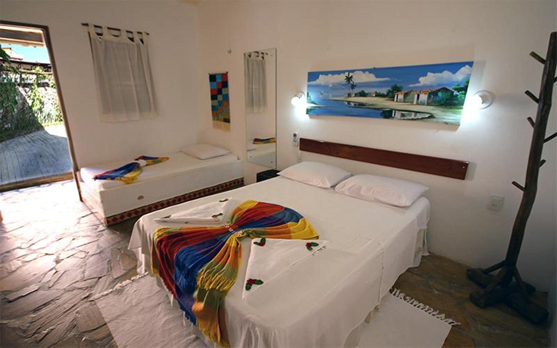 Een slaapkamer met een bed, een schilderij, een kapstok en een raam met gordijnen.