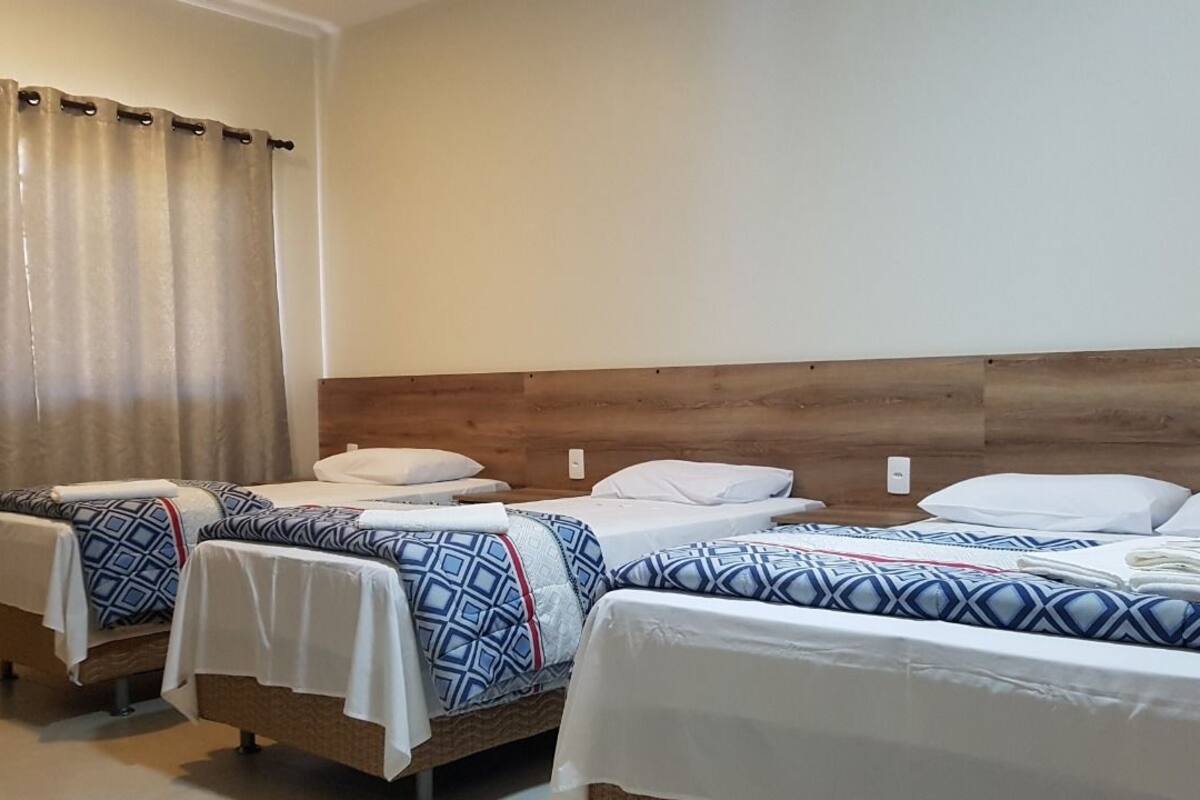 Une chambre d’hôtel avec trois lits, chacun doté de draps à motifs et d’oreillers blancs.