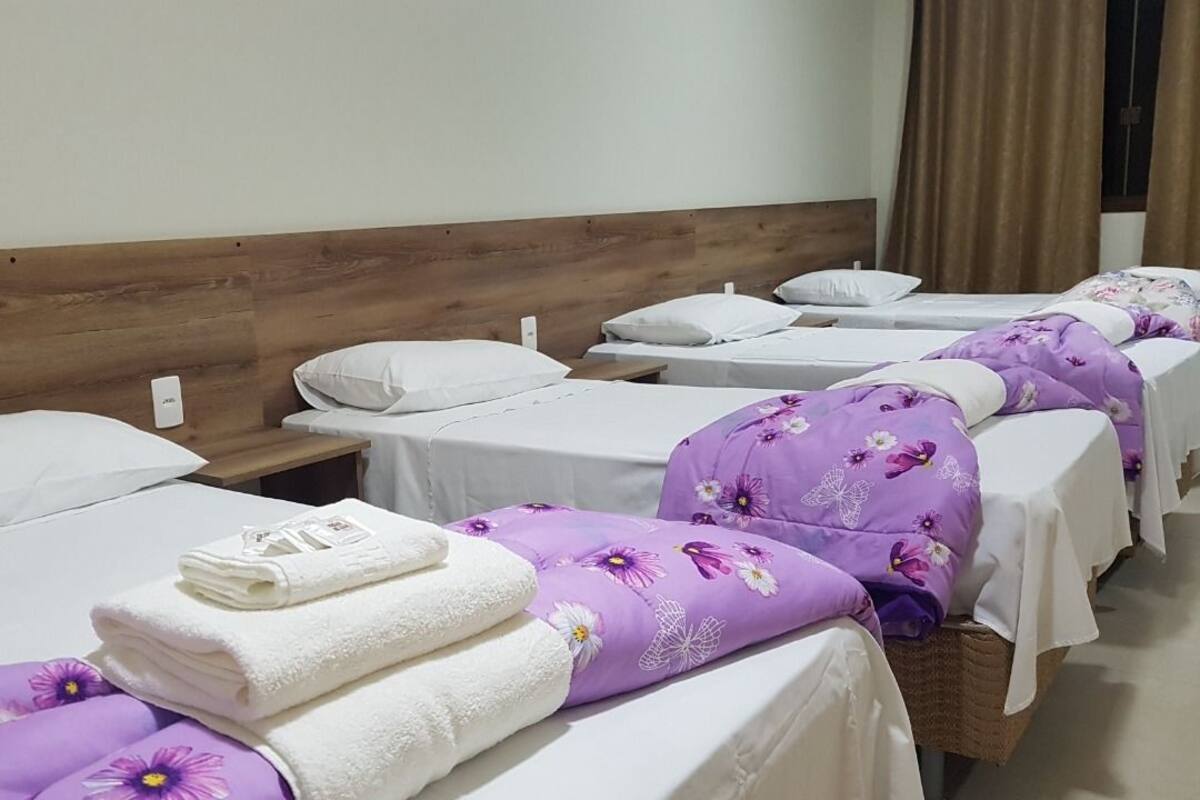Une rangée de lits simples avec des têtes de lit en bois, du linge de lit blanc et des couvertures à motifs floraux violets.