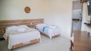 Ein Hotelzimmer mit zwei Betten, einem hölzernen Kopfteil, einer kleinen Küchenzeile und einem durch eine offene Tür einsehbaren Badezimmer.