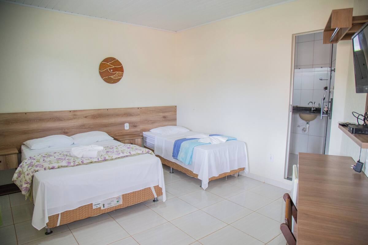 Une chambre d’hôtel avec deux lits, une tête de lit en bois, un petit coin cuisine et une salle de bain visible à travers une porte ouverte.