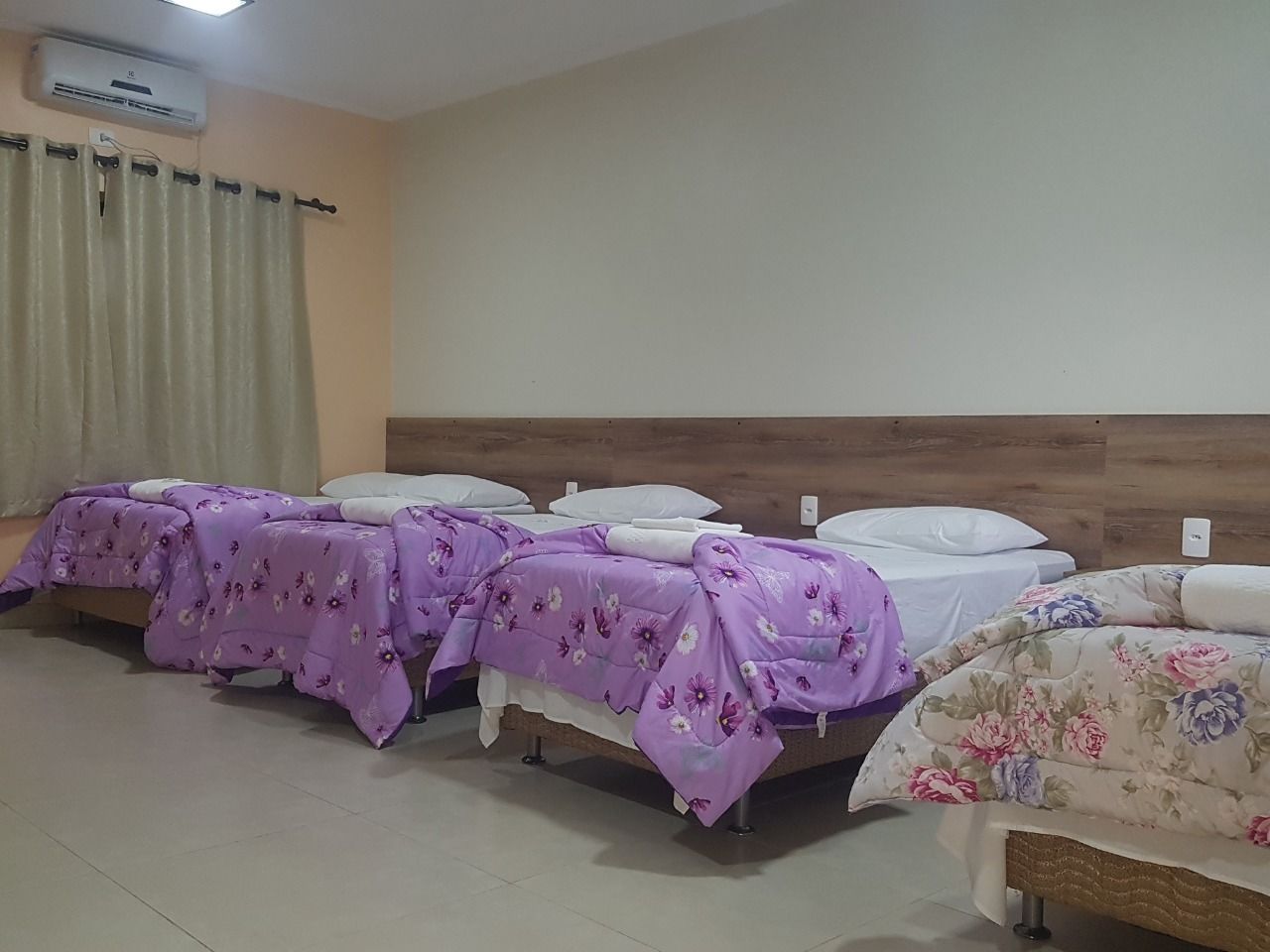 A hotel room with four beds, each with a floral bedspread.