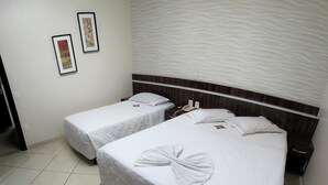 Une chambre d’hôtel avec deux lits simples, un grand lit et une tête de lit au motif texturé.