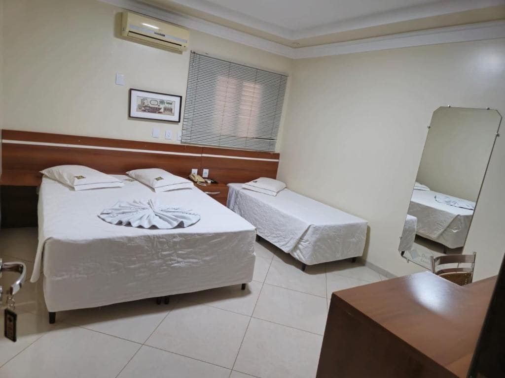 Habitación de hotel con dos camas, una mesita de noche, un espejo y una ventana con persianas.