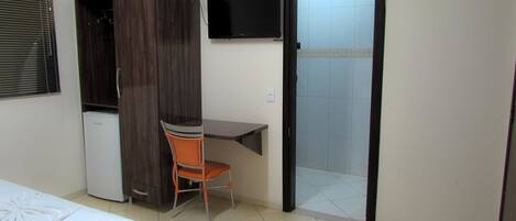 A room with a bed, a desk, a chair, a television, and a door.