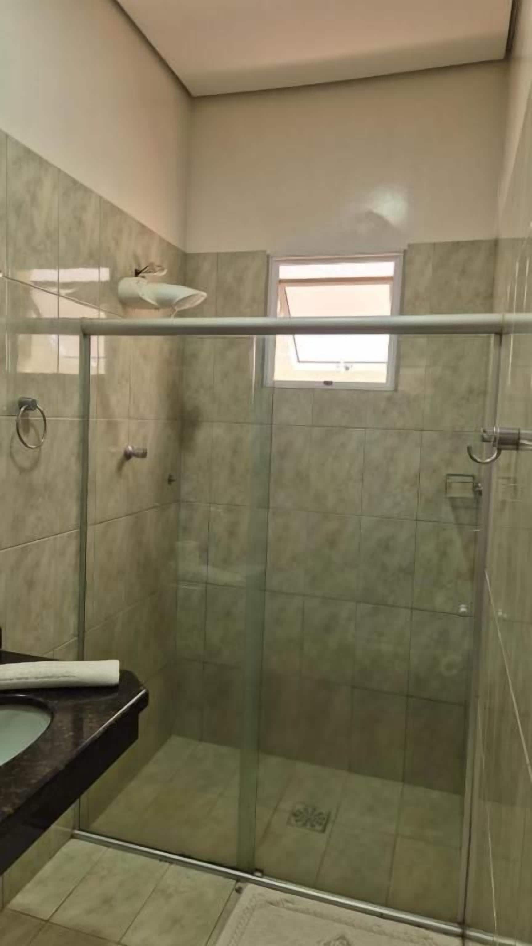 A bathroom with a glass-enclosed shower, a sink with a dark countertop, and a window providing natural light.