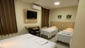 A hotel room with a large bed, two smaller beds, a desk with a chair, a flat-screen TV, and an air conditioning unit. - Palace Hotel Angra (Angra dos Reis)