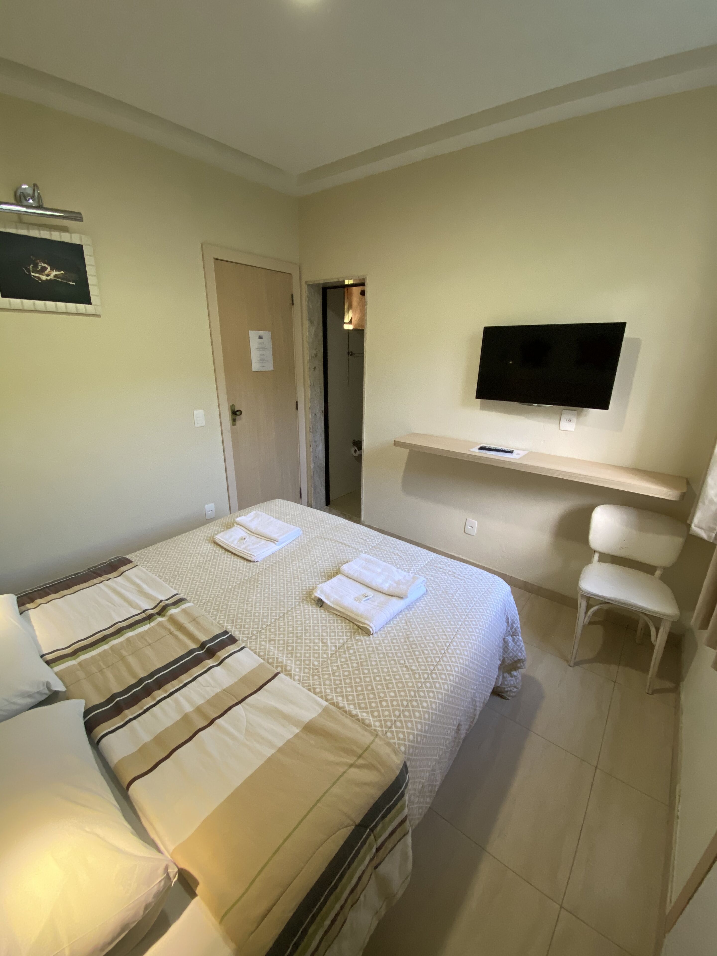 Una habitación de hotel con dos camas, un televisor montado en la pared, una silla y una puerta que da a otra habitación.
