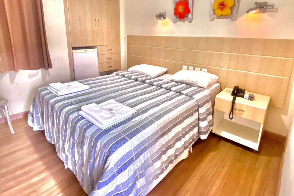 A hotel room with a bed, bedside table, and a wall-mounted air conditioning unit.
