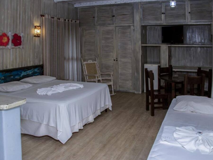 Quarto de hotel com duas camas, uma cadeira, uma mesa e uma televisão.