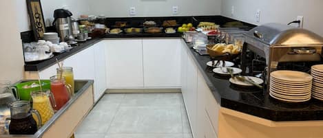 A hotel kitchen with a buffet setup, including a coffee station, fruit, and various food items.