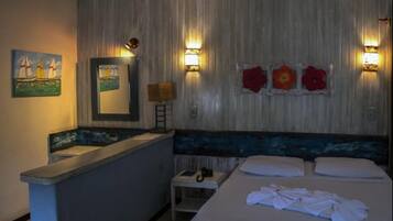 A hotel room with a bed, a small desk with a lamp, a mirror, and artwork on the walls.
