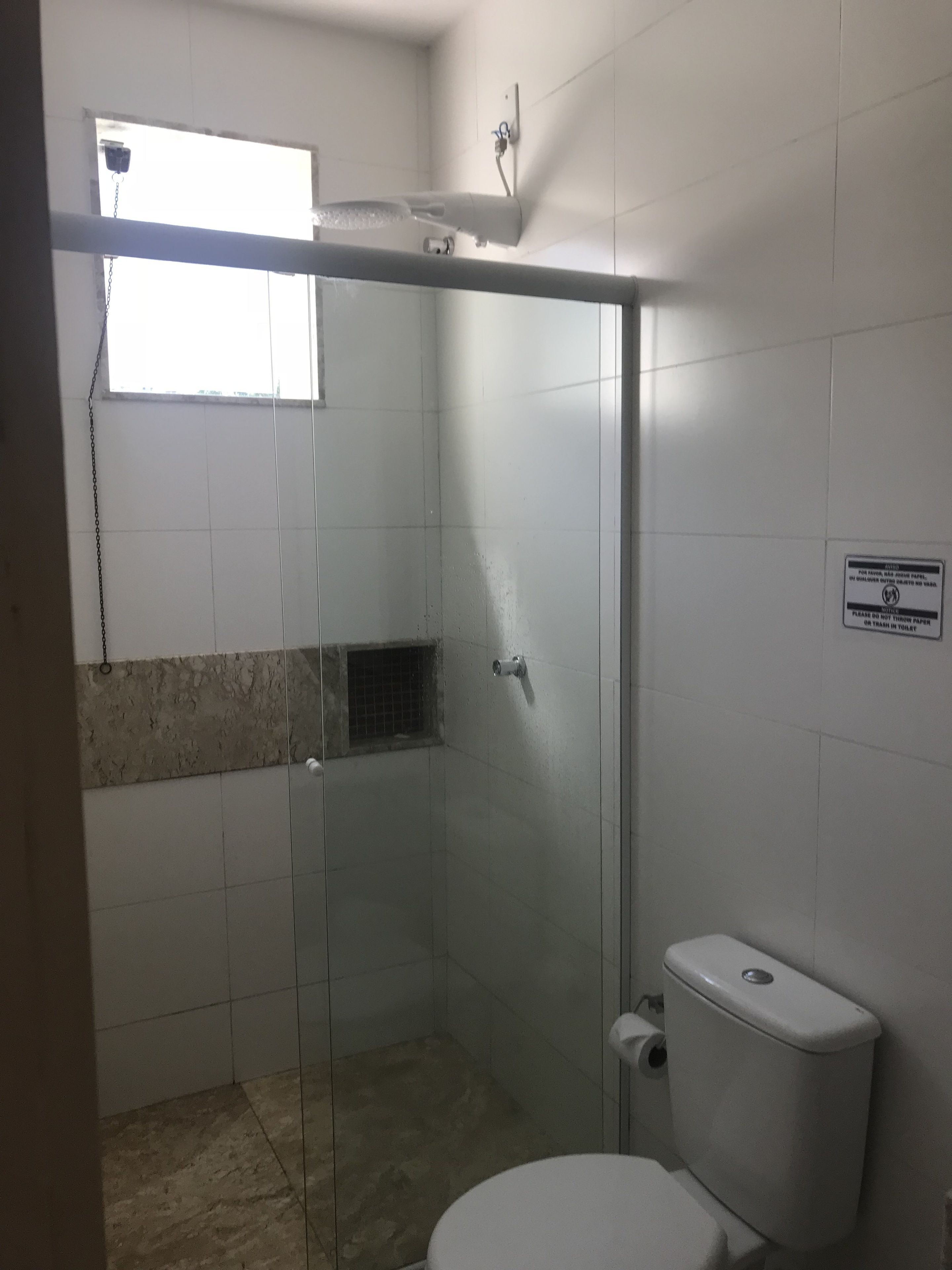 Un baño con cabina de ducha de vidrio, inodoro y ventana.