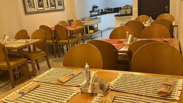 Un comedor con mesas y sillas de madera, una cocina al fondo y una obra de arte enmarcada en la pared.