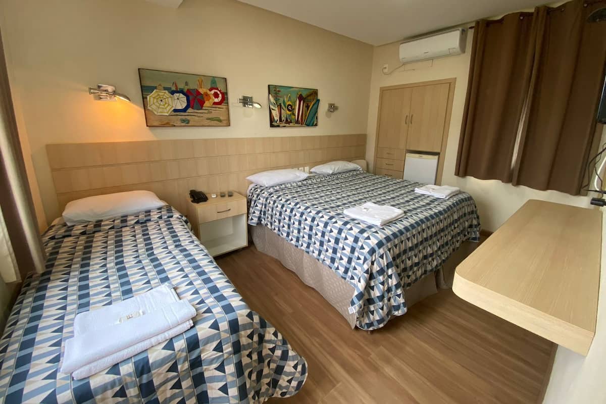 A hotel room with two beds, a desk, a wardrobe, and two wall-mounted artworks.