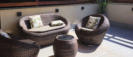 A patio with wicker furniture, a large umbrella, and a potted plant.