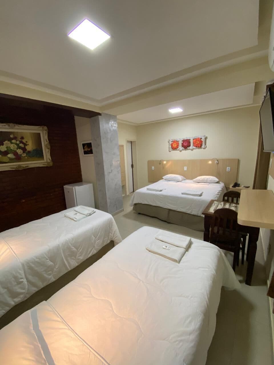 A hotel room with two single beds, a desk, a chair, a small refrigerator, and a painting on the wall.