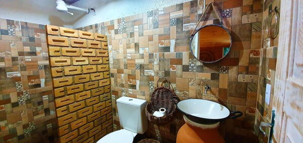 A bathroom with a tiled wall, a toilet, a sink, and a mirror. - Vila Aju Pousada Temática (Aracaju)