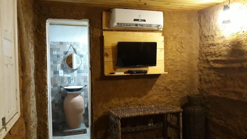 Un baño rústico con pared de piedra, un estante de madera con un televisor, un espejo y un jarrón grande.