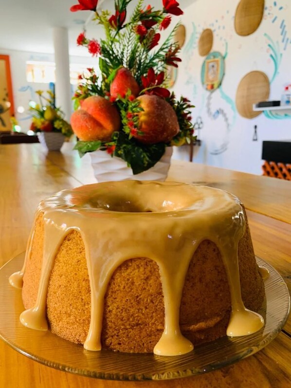 A bundt cake with caramel glaze on a glass plate on a wooden table. - Vila Aju Pousada Temática (Aracaju)