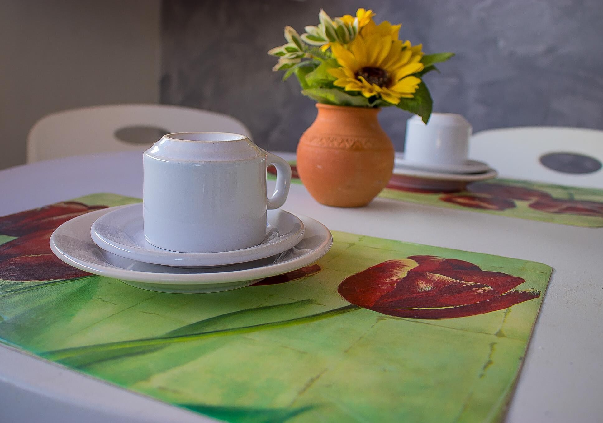 Una taza y platillo blancos sobre una mesa con un mantel individual estampado con flores.